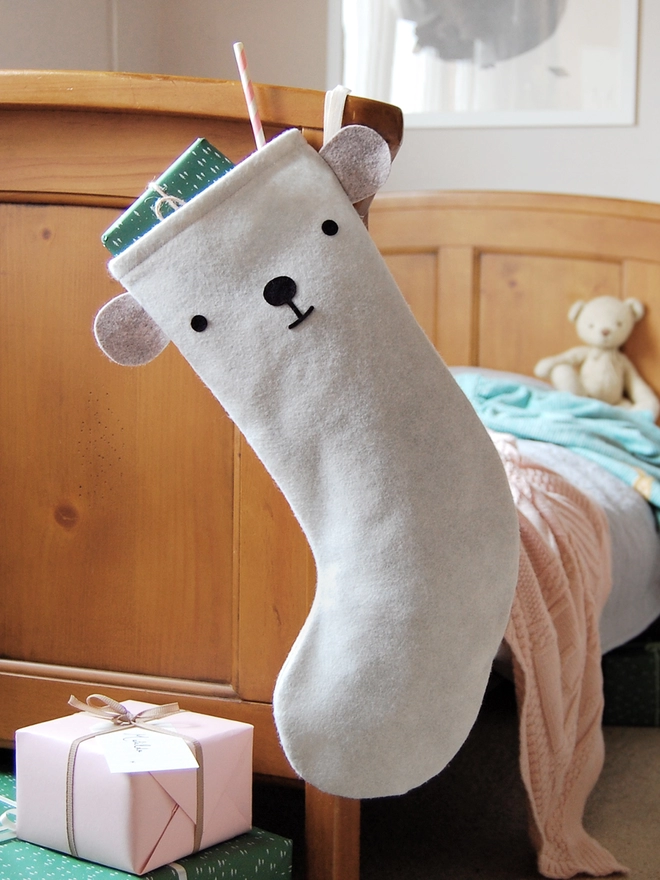 A handmade felt polar bear stocking hangs on the end of a wooden bed.