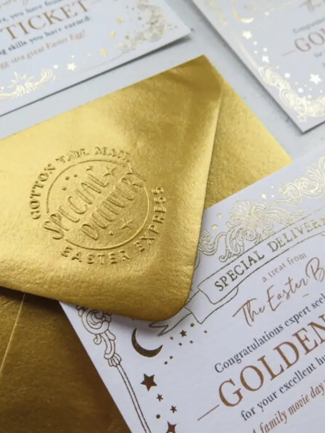 Close-up of the embossed "Special Delivery" stamp on the flap of the metallic gold envelope. The corner of a Golden Ticket with gold foil stars and a crescent moon rests beside it.