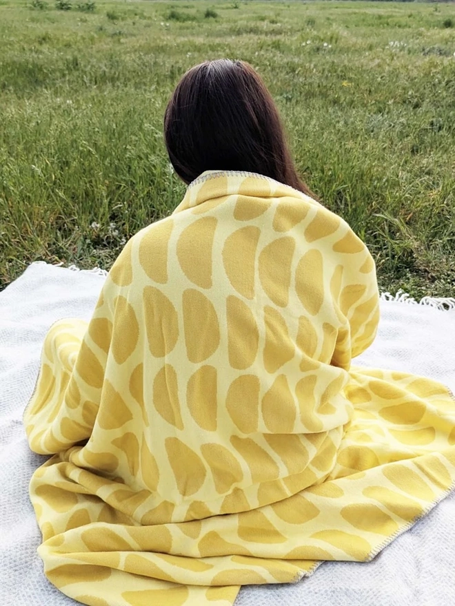 Organic Cotton Throw, a woman sitting with a throw draped on her outside. 