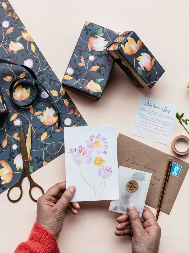 Liz Temperley's printed Candytuft Card seen with accompanying wildflower seeds. Behind is Liz Temperley's wrapping paper.