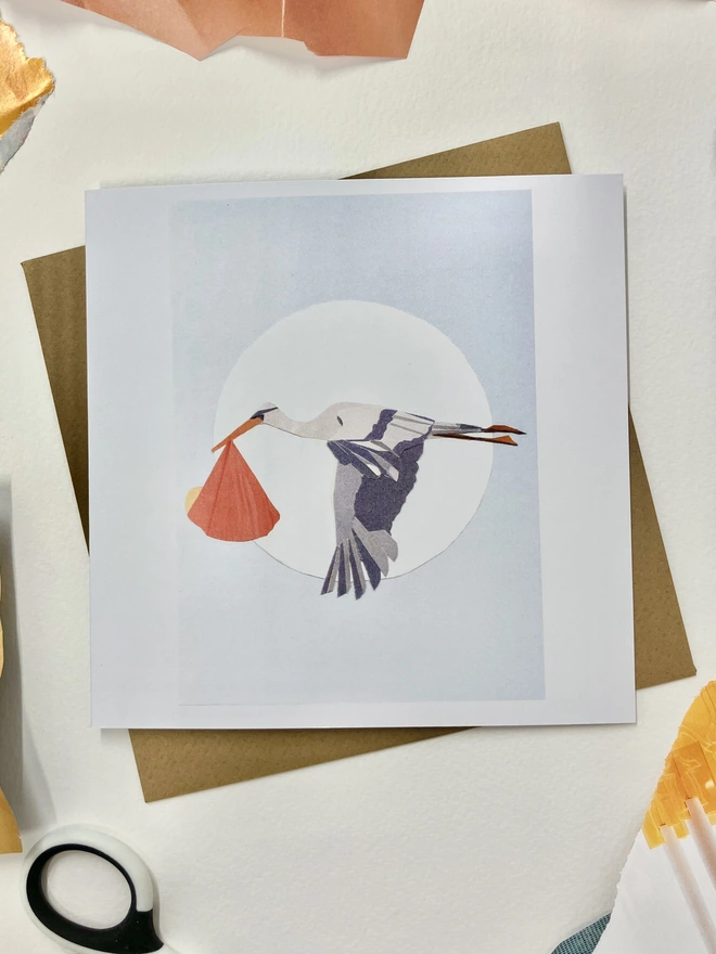 Collage of a stork delivering a newborn baby greetings card and envelope on a background of collaging materials