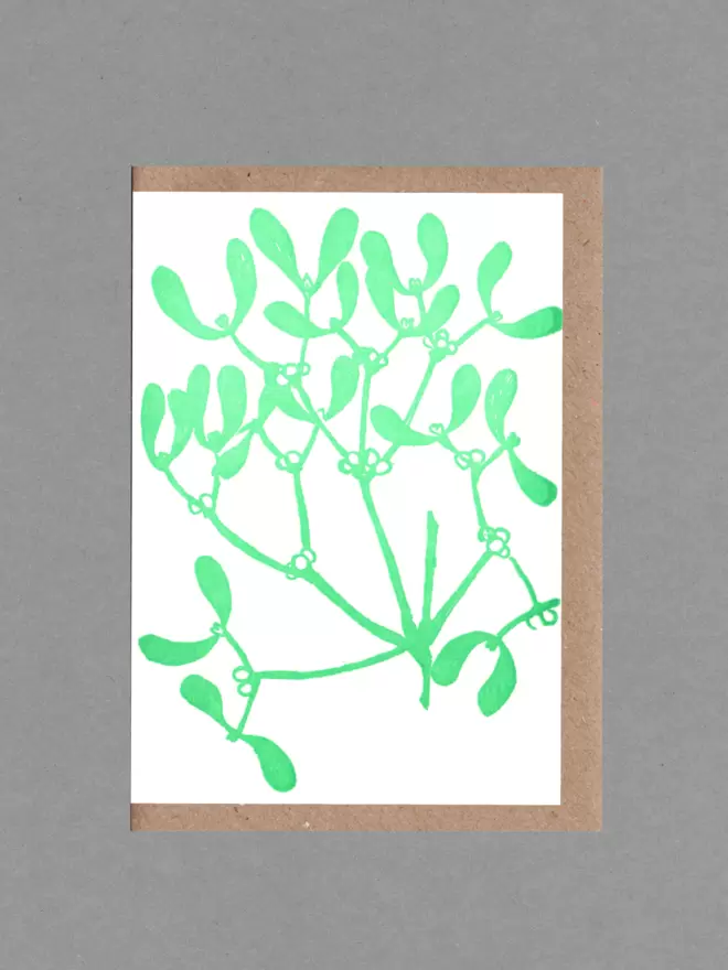 A greetings card with an illustration of mistletoe in bright green. Behind the card is a brown envelope on a grey backround.t 