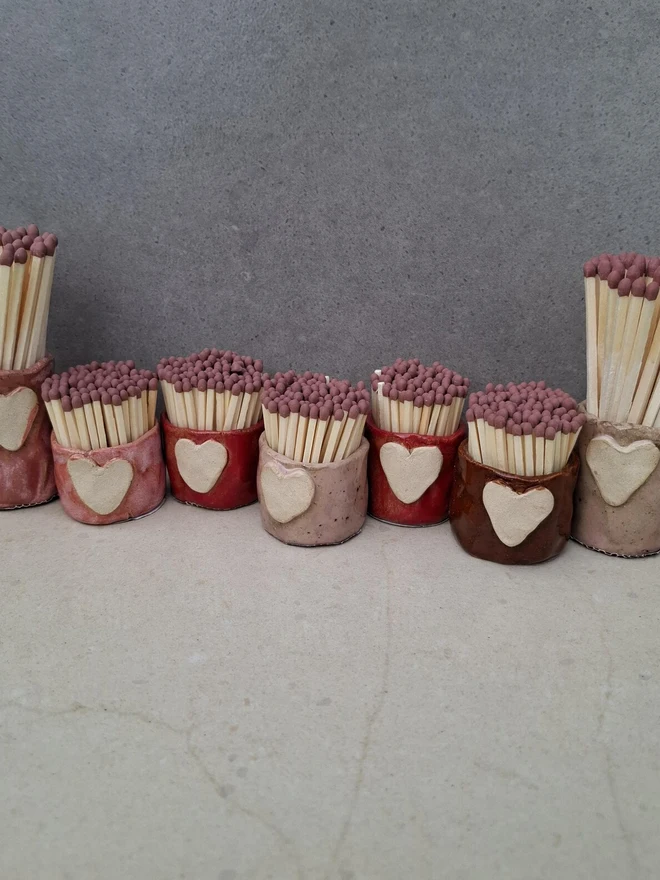 Heart Design Handmade Ceramic Match Holder & Strikers, row of colourful match holders against a plain background on a white surface. 