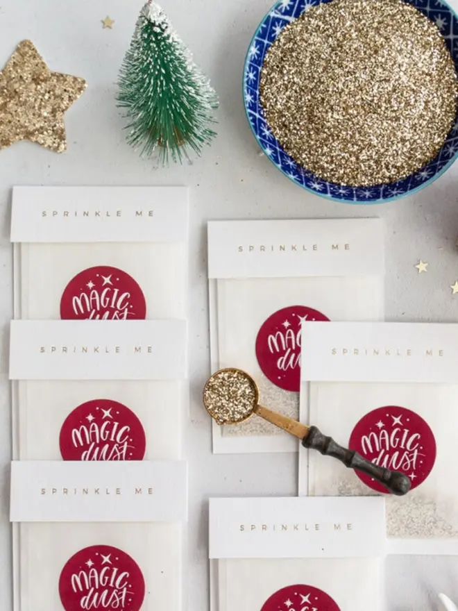Glassine "Sprinkle Me" Magic Dust packets beside a bowl of gold glitter and a brass scoop.