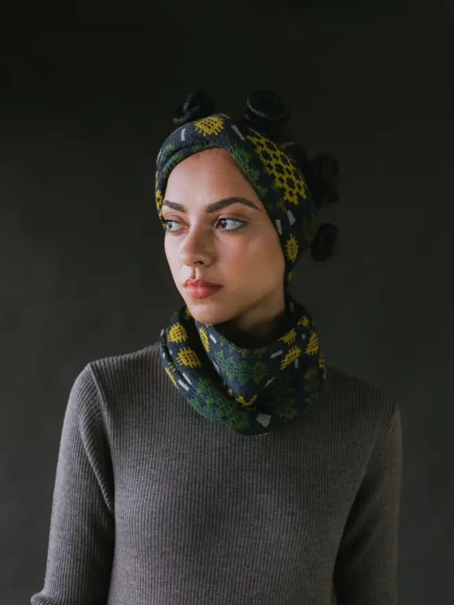 Model wearing pieces from MABLI's 'Carthen' collection, featuring the Carthen Wrap in the vibrant 'Anthracite/Pea' colour-way. The design showcases bold, colourful patterns inspired by traditional Welsh blanket tapestry.