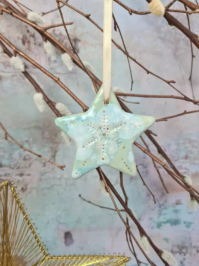 Star Christmas decorations, ceramic decorations, dream catcher, christmas star, pottery, Jenny Hopps Pottery, J.H Pottery, J.Hopps Pottery, Clay star, gift, christmas tree, blue with white and cream with gold details, on a light gold ribbon, photographed on a branch with Christmas lights