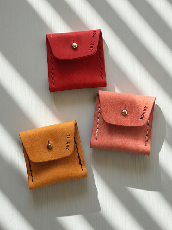 3 leather coin purses against a white back ground. Each stamped with a name.