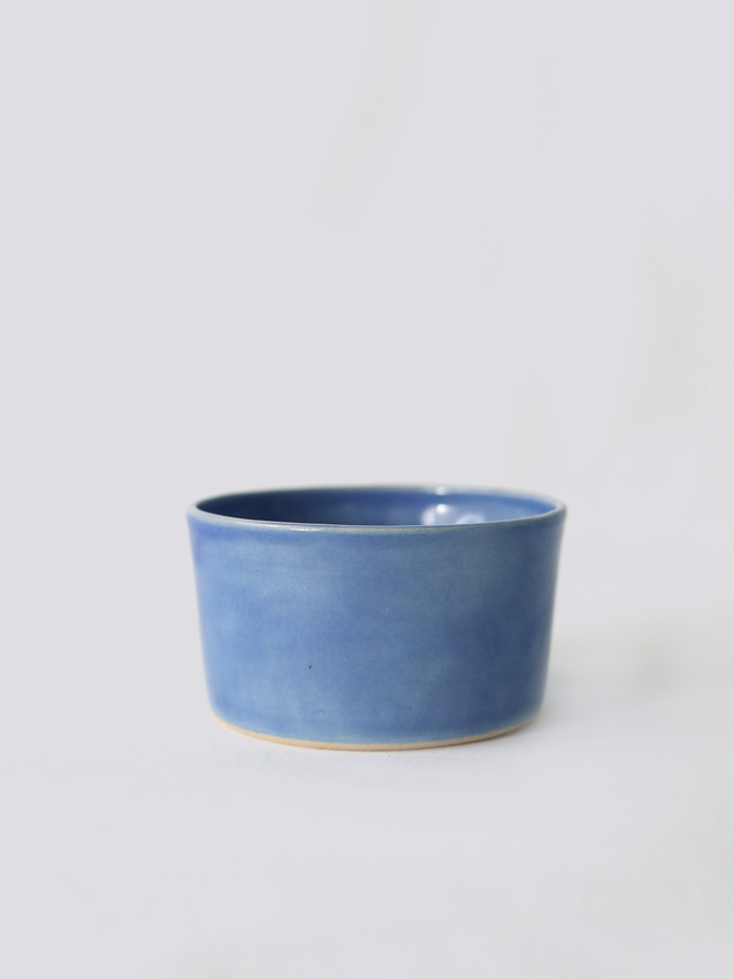 A small handmade ceramic side bowl in glossy pacific blue glaze, with a tapered sides and a wide open rim, photographed against a plain light grey background
