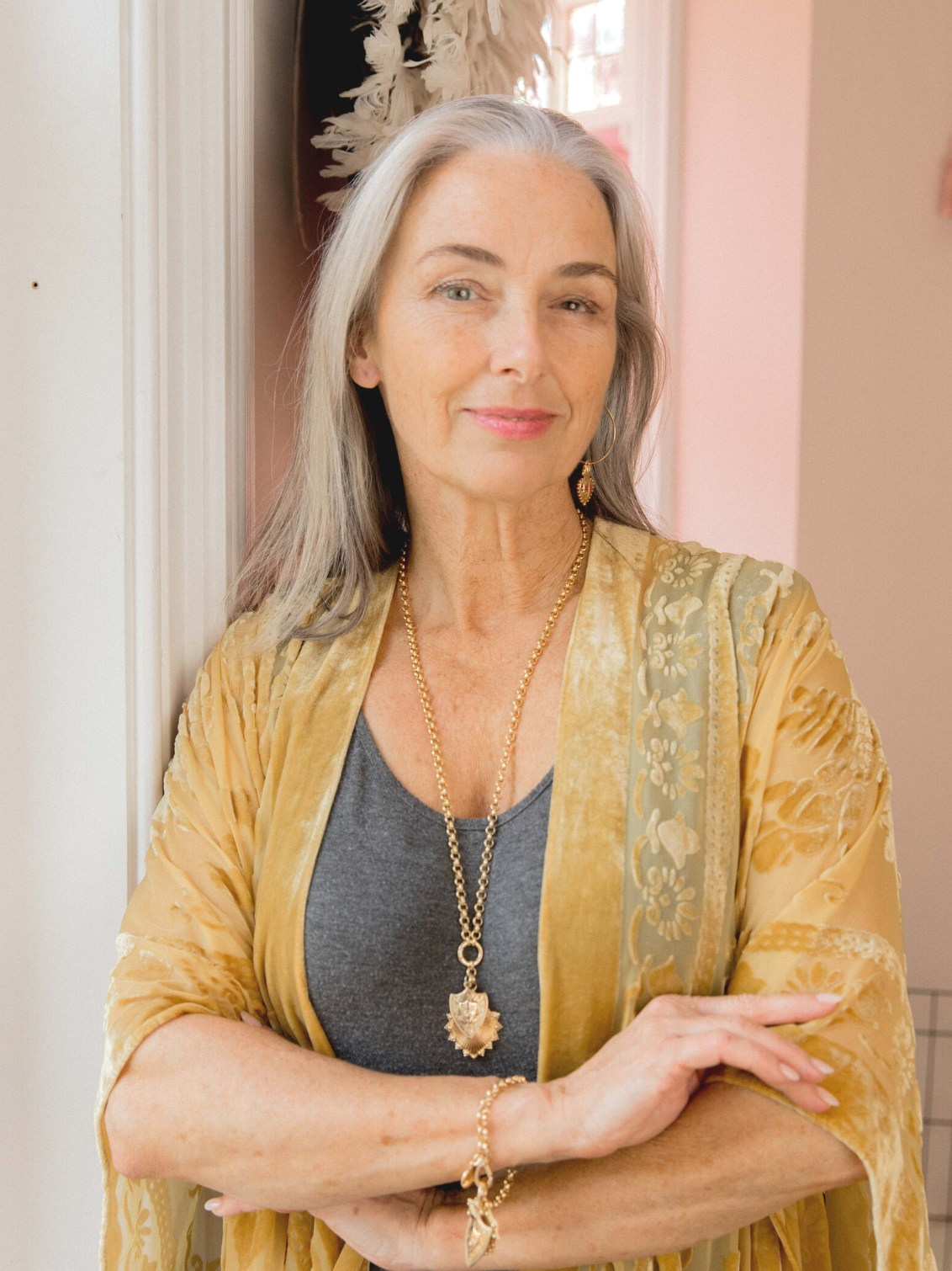 Grey haired woman wearing a yellow kaftan and a gold belcher chain necklace with a gold Joan of Arc shield charm