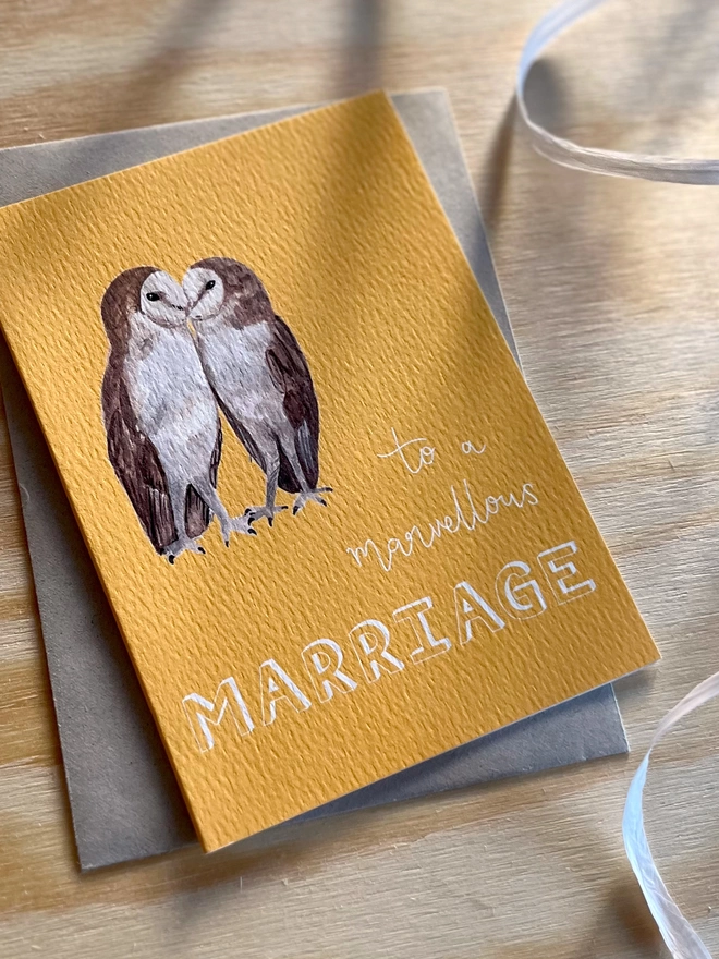 a greetings card with a bright yellow background featuring two kissing barn owls and the phrase ‘to a marvellous MARRIAGE”