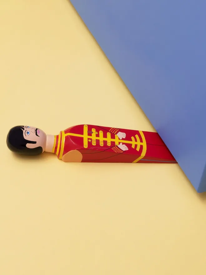 Wooden Door Stopper (Starky), a colourful wooden door stop sitting under a door.