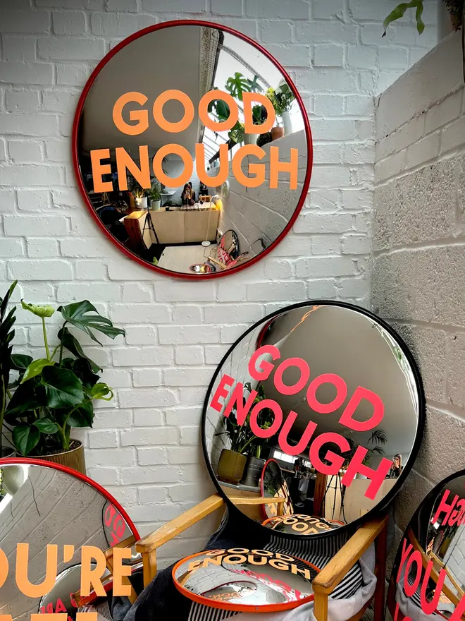 Group shot of round convex mirrors - all handpainted in neon pink or orange against a white brick wall with house plants