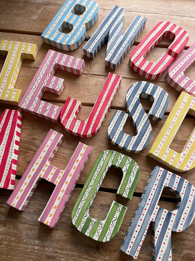 Several colorful striped decorative letters arranged on a wooden table.