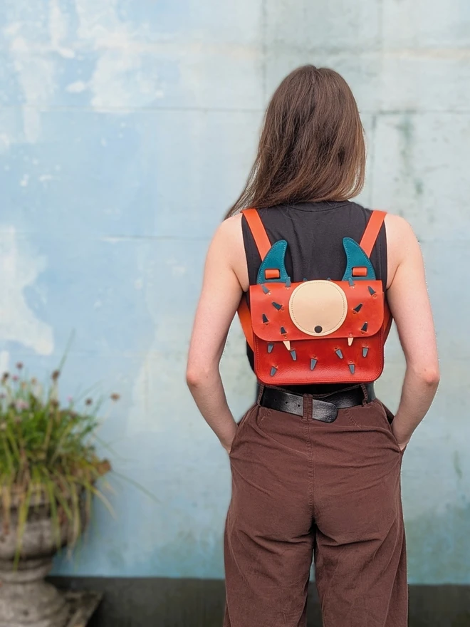 Leather monster backpack in orange and blue worn by female model.