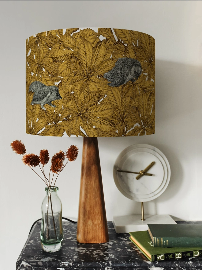 Handmade lampshade featuring cosy hedgehogs nestled among autumnal yellow leaves, creating a warm and whimsical woodland design.