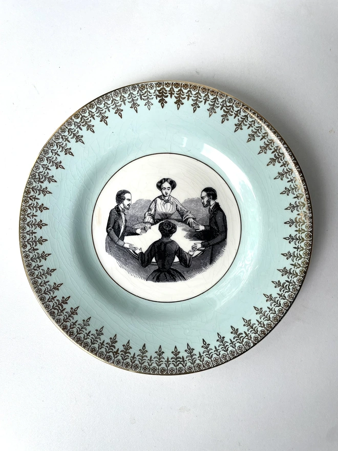 a vintage plate with ornate border has the vintage illustration of 2 men and 2 woman holding a seance at a table