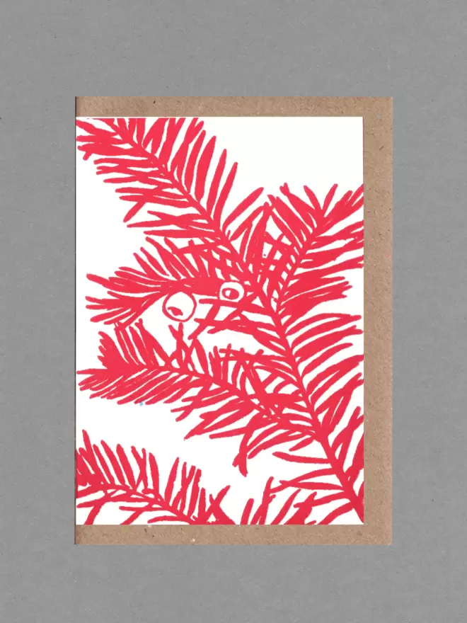 Greetings card with an illustration of a yew branch in bright red. Behind the card is a brown envelope on a grey back round.