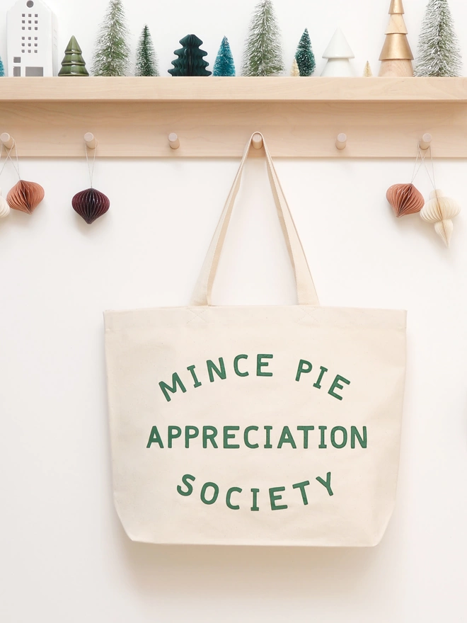 a large natural canvas tote bag bearing the words mince pie appreciation society hanging on a hook