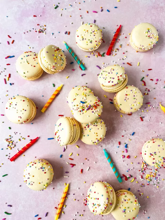 white macarons with sprinkles on a pink background with colourful sprinkles and candles