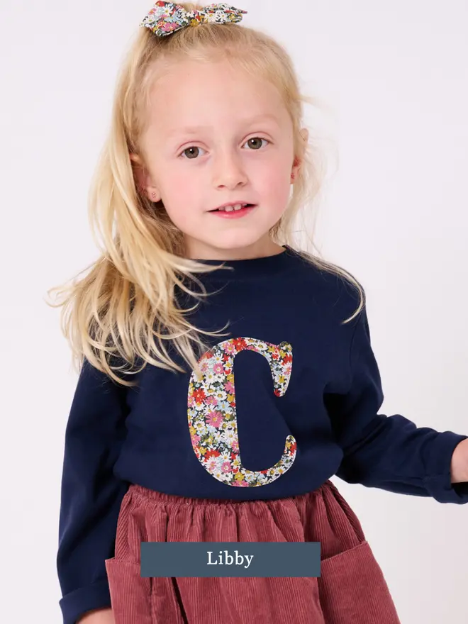 a 3 year old girl wearing a personalised kids personalised navy t-shirt with an initial cut from Libby liberty floral print on the front