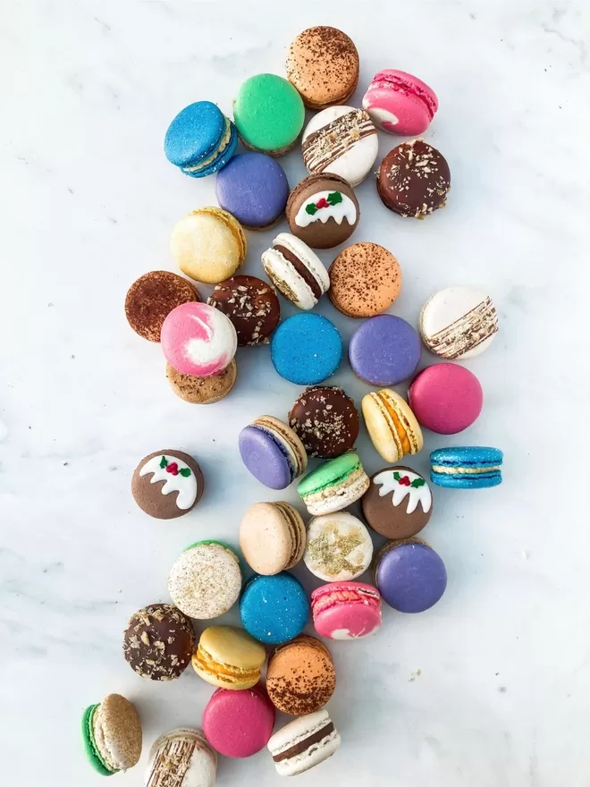 many different coloured Christmas macarons on a white marble surface