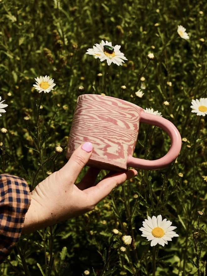 Herringbone Chunky Mug, a colourful mug held above a grassy backdrop. 