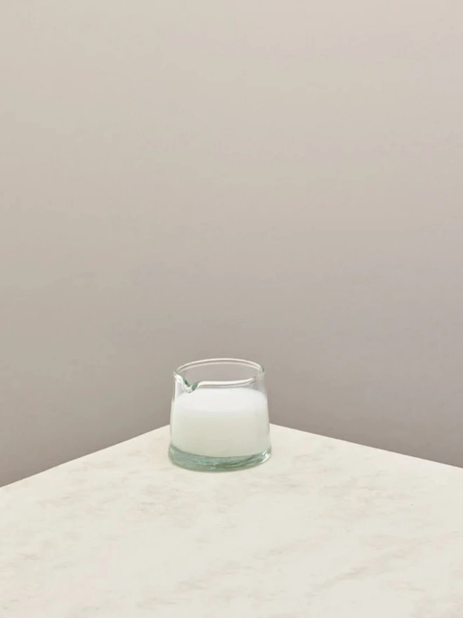 Low Jug, a small glass jug sitting on a counter top against a plain backdrop. It is filled by milk. 