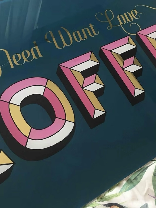 'Need Want Love Coffee' Gold Glass Sign, a gold glass sign hanging on a white brick wall. 