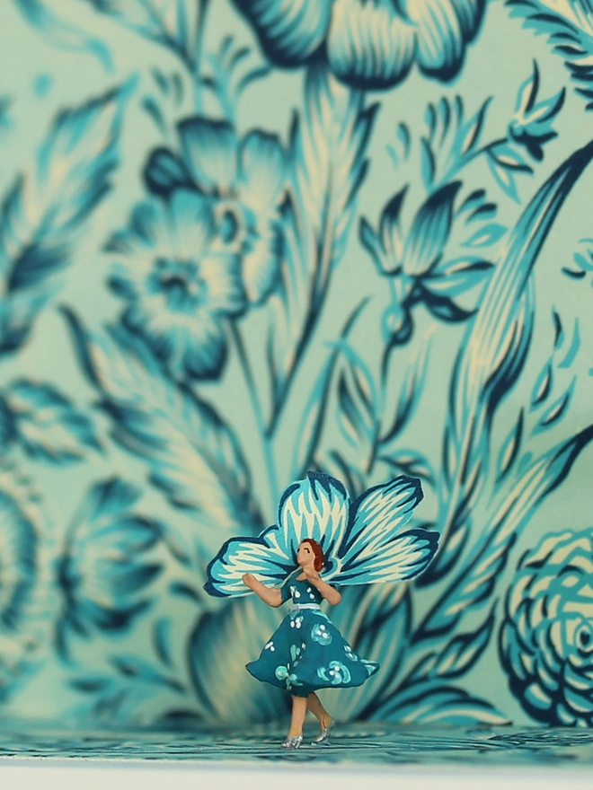 Miniature scene in an artbox showing a tiny lady in floral dress almost disappearing against matching floral wallpaper - close up