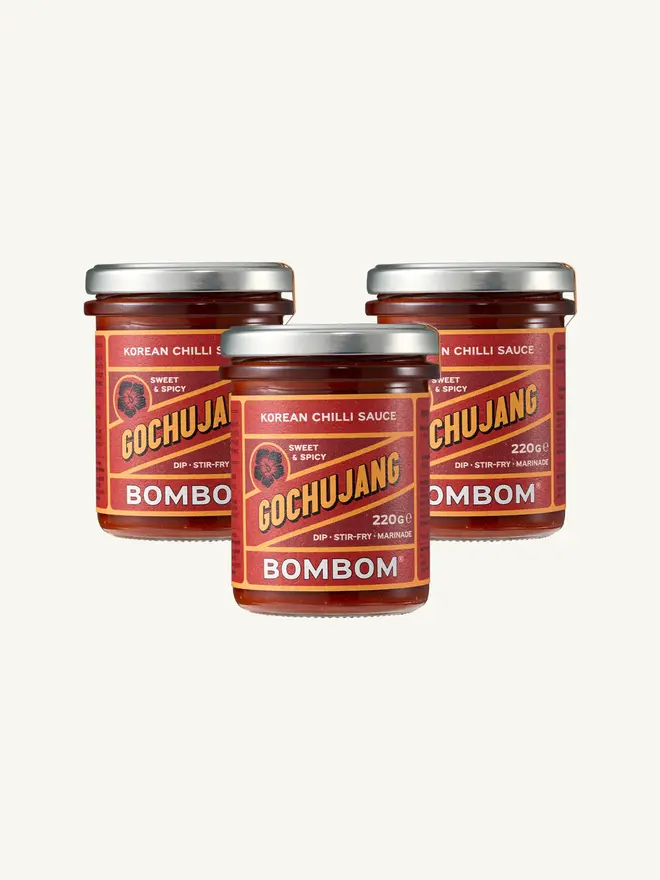 korean gochujang chilli paste. three jars of gochujang paste photographed against a red background.