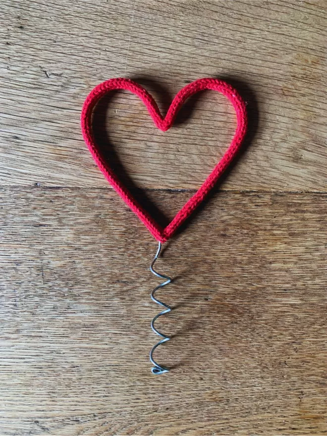 A red string wrapped wire heart shaped Christmas tree topper on an oak table