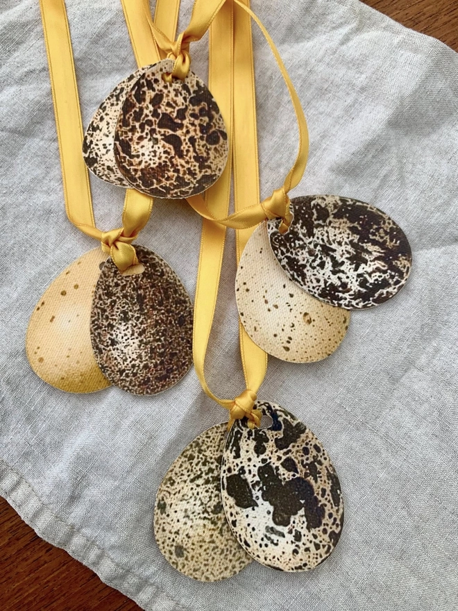 a set of four napkin ties with speckled eggs and gold ribbon