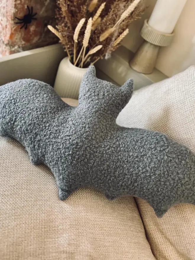 boucle bat pillow. a grey cushion shaped like a bat.
