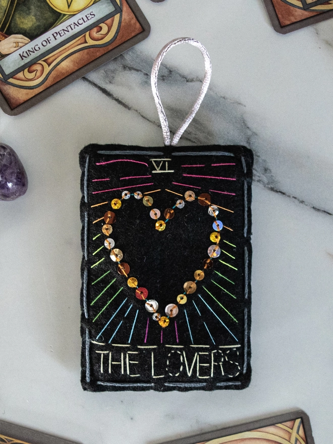 A handcrafted felt ornament with sequins and embroidery depicting "The Lovers" tarot card