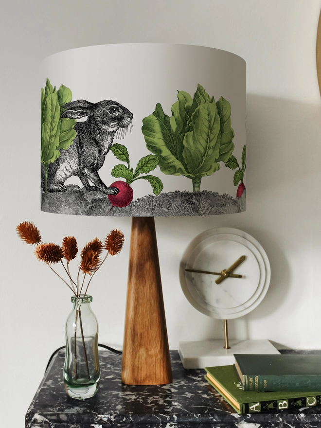 Peter Rabbit inspired Drum Lampshade featuring a Rabbit among lettuces and radishes on a wooden base on a shelf with books and ornaments