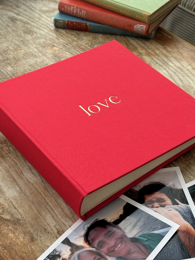 on a wooden table there is a photo album which has the word 'love' printed on the front. It is surrounded by photos of family and friends.