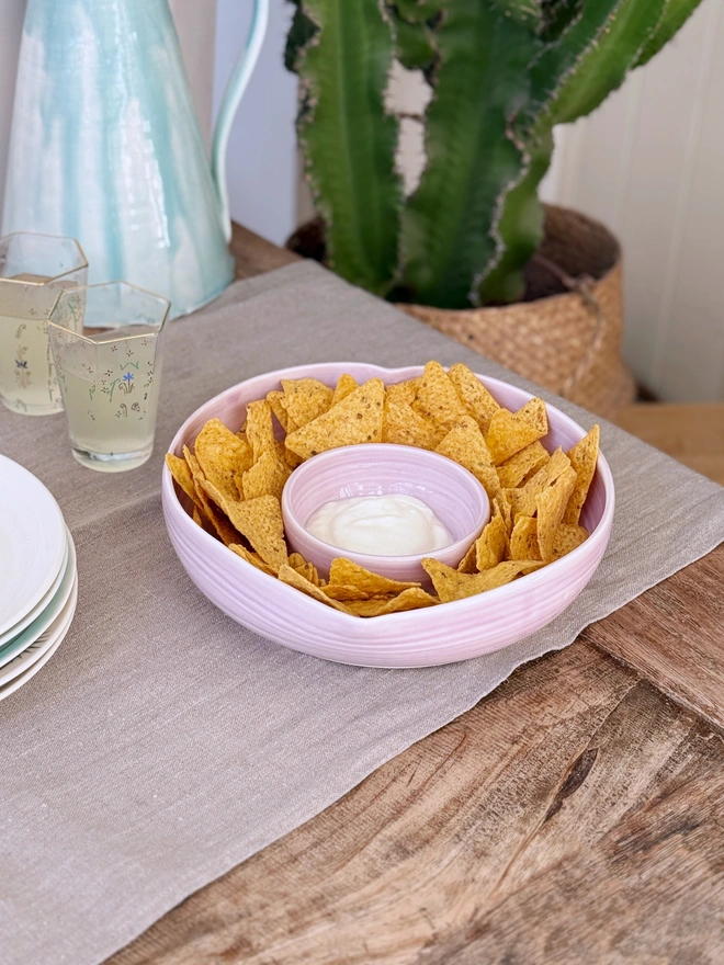 Heart shaped chip and dip bowl with tortilla chips and dip on a rustic wooden table