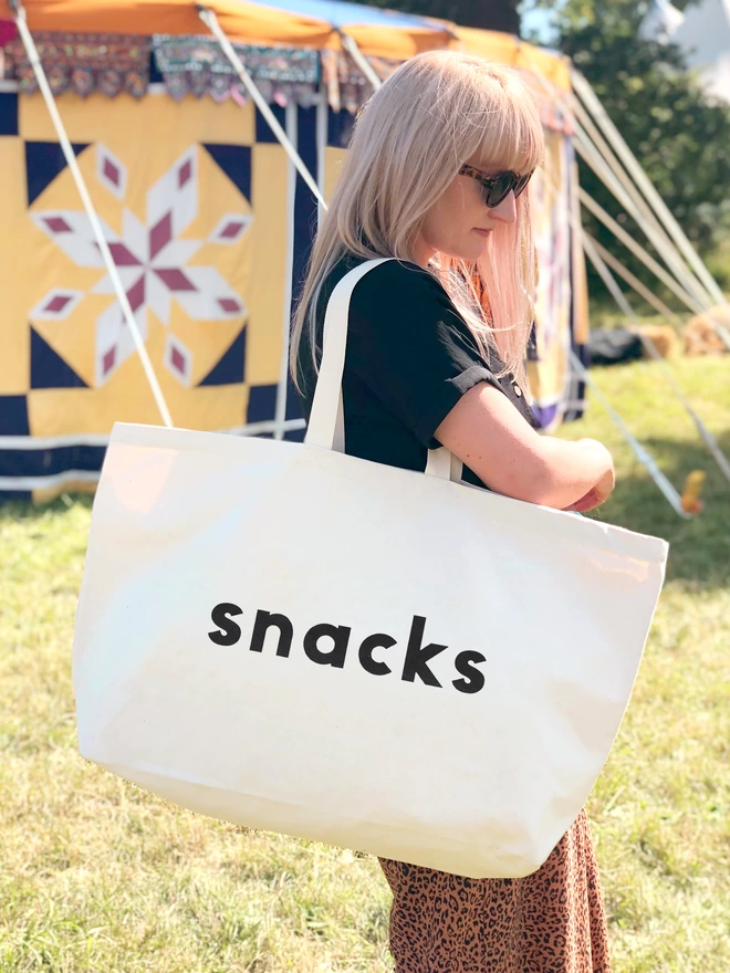 model holding an oversized natural canvas tote bag with bold snacks slogan