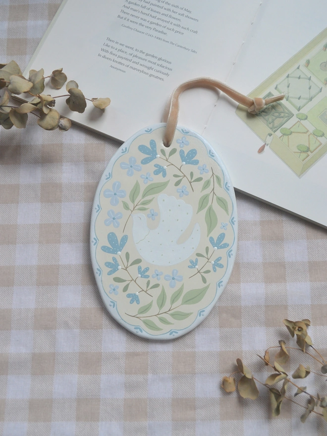 oval ceramic decoration with white dove illustration and blue and green floral decor