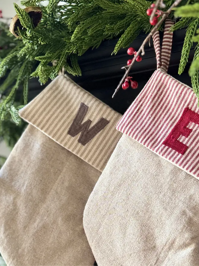 Striped Embroidered Christmas Stocking. two stockings hanging from a mantle with block letters on the striped cuff