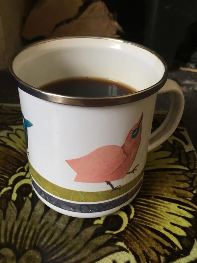 Enamel mug decorated with pionk bird standing on a green patterned tile