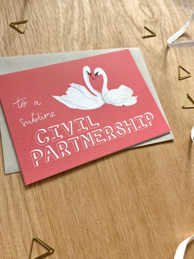 a greetings card with a deep pink background featuring two swans with their necks meeting in a heart shape, and the phrase “to a sublime CIVIL PARTNERSHIP”