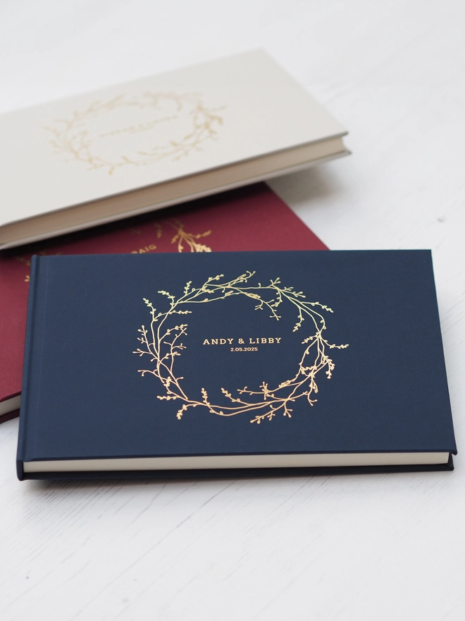 Personalised Wedding Guestbook. A personalised hardcover wedding guestbook with a delicate gold vine wreath illustration on the front and personalise with names and a date. 