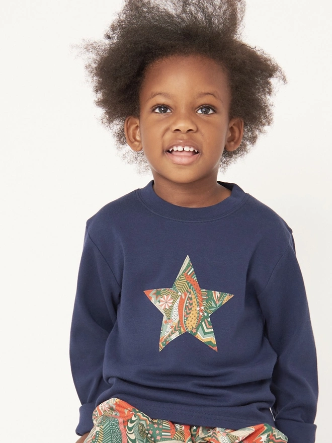 A 4 year old boy wearing a navy blue christmas tee with a Liberty star print star sewn on the front