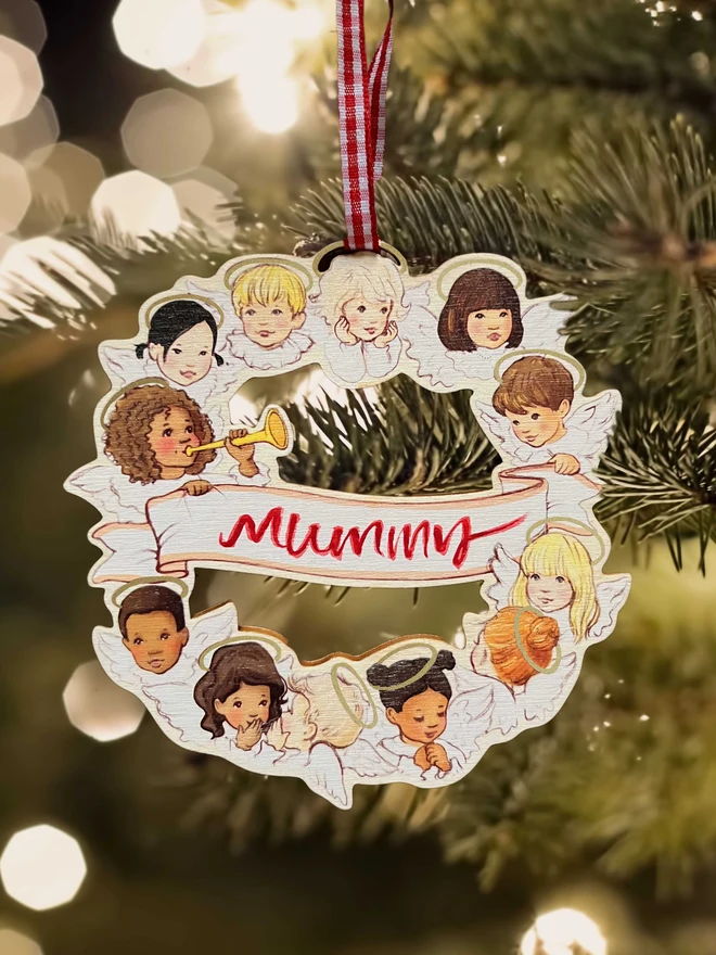 a wooden angel wreath hung in a Christmas tree featuring my original illustration of a circle of angels