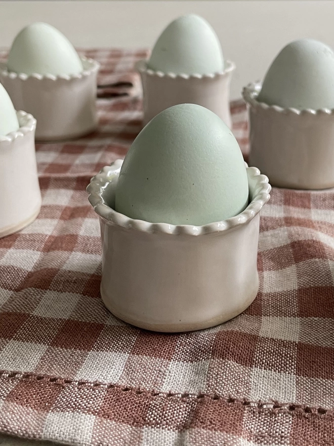 side view of egg cups with eggs in on a brown checked placemat