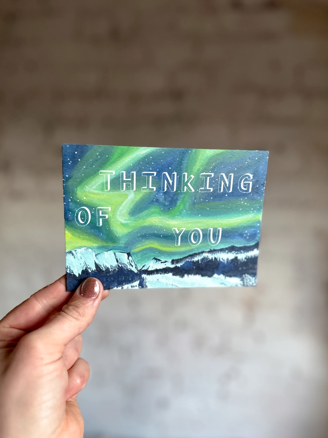a greetings card featuring an illustration of the northern lights landscape with the text “thinking of you”