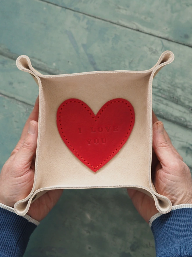 Personalised love heart leather anniversary coin tray. A natural cream square leather tray with a red heart stitched to the middle. The love heart has been stamped with the phrase 'I LOVE YOU'