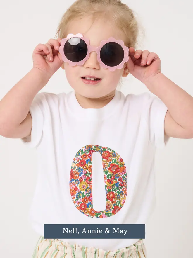 a 2 year old girl wearing a personalised kids white t-shirt with an initial cut from liberty floral print on the front