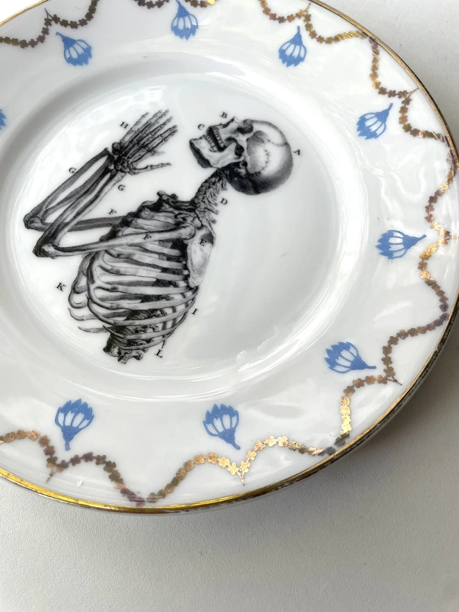 a vintage ornate plate that has a patterned border, and in the centre i have print a black and white illustration of praying hands skeleton in a vintage style